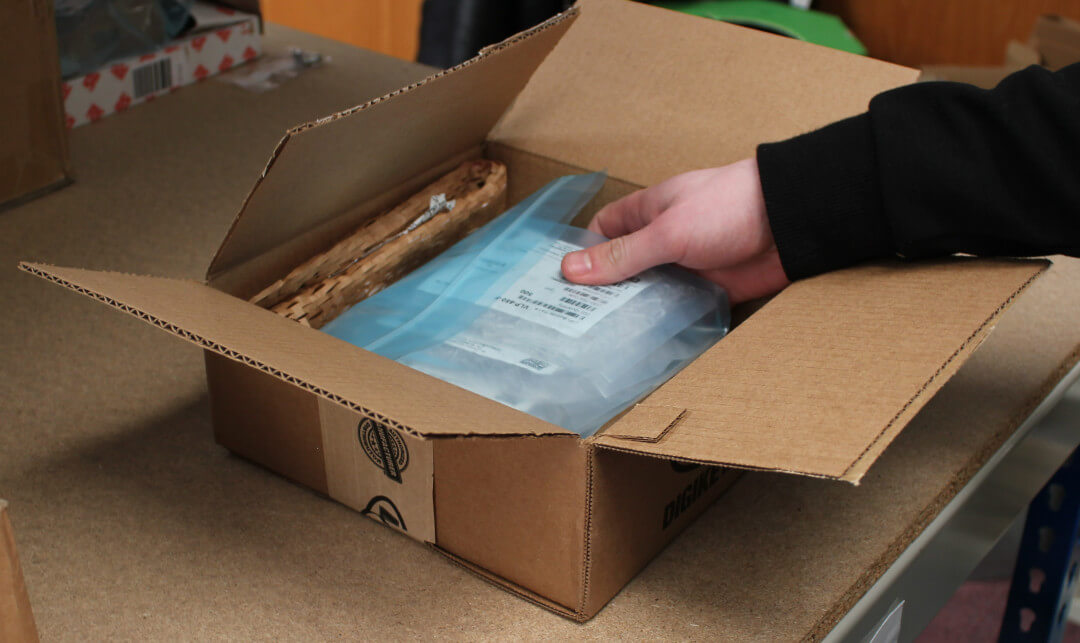 A hand reaching into an open cardboard box to pick up a plastic-sealed product.