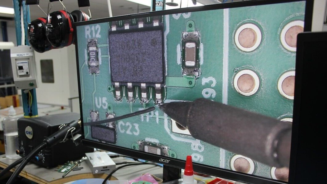 Magnified view of hand soldering on a computer monitor.