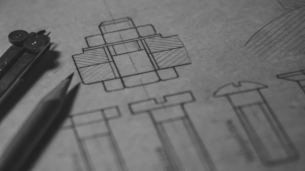 A closeup of a mechanical design blueprint with a sharp pencil and compass resting alongside it.